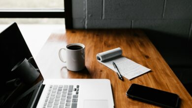 Notebook, caderno e xícara sobre uma mesa de trabalho